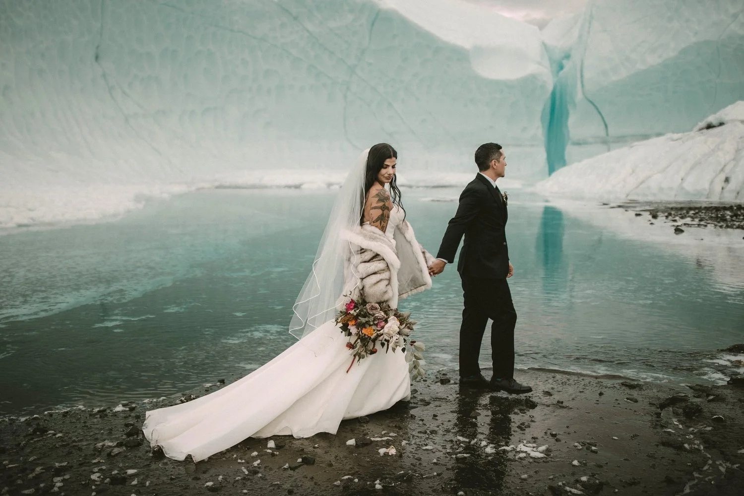 A couple stands on a blue Alaskan glacier under misty mountains